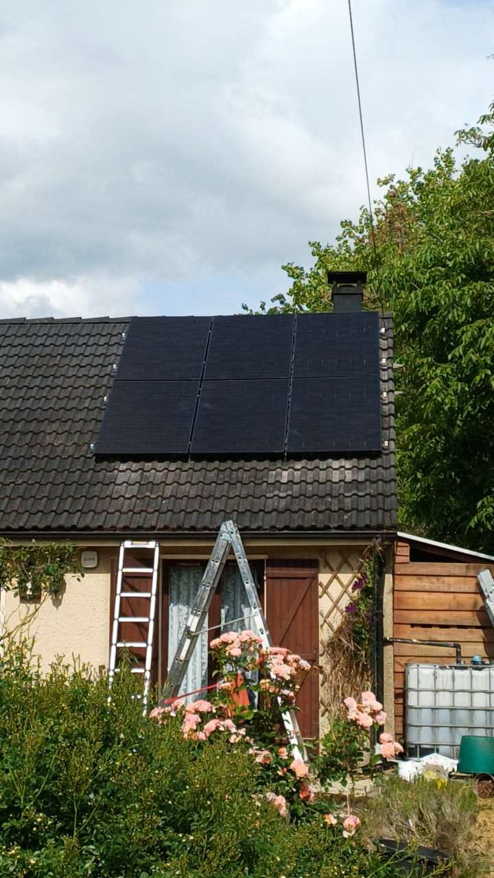 Vue depuis le jardin d'une maison équipée de panneaux photovoltaïques, rosiers en premier plan
