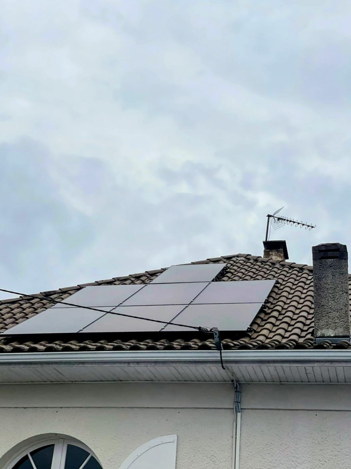 Panneaux photovoltaïques installés sur une toiture en tuiles canal sous un ciel couvert, souche de cheminée et antenne visibles