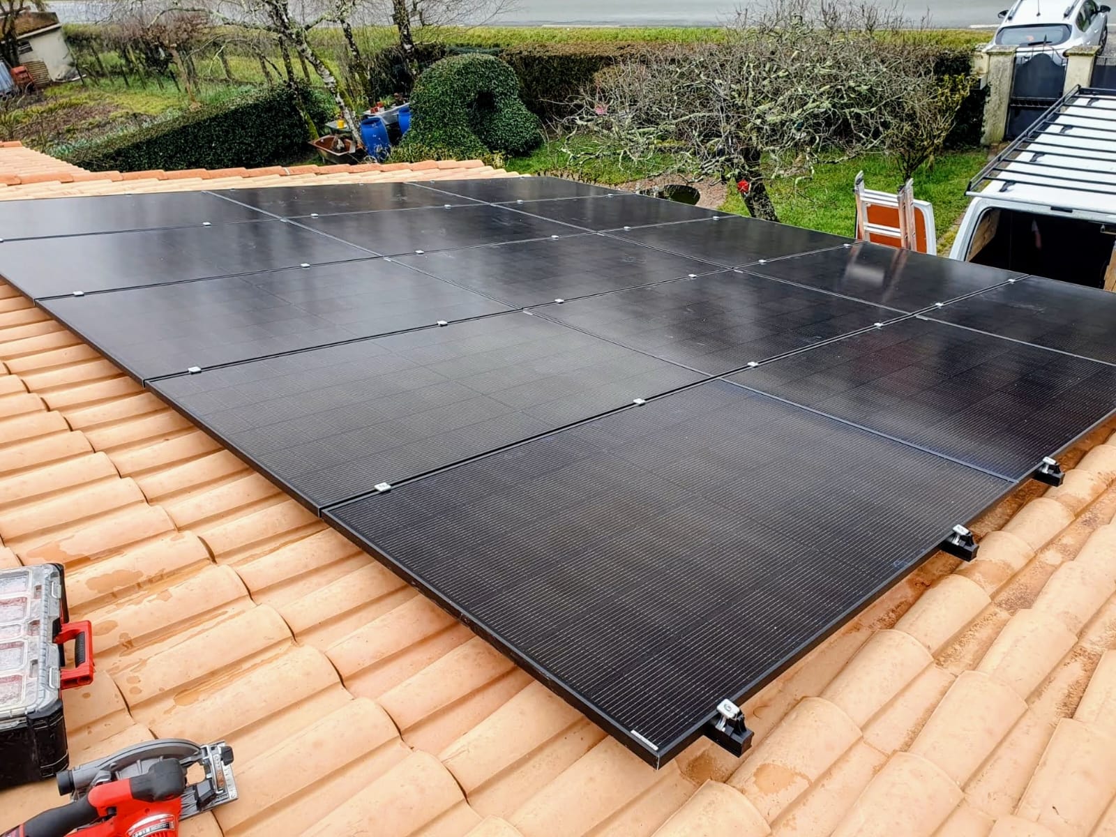 Pose de quinze modules photovoltaïques full black sur une toiture en tuiles canal, outils et visseuse posés sur la couverture