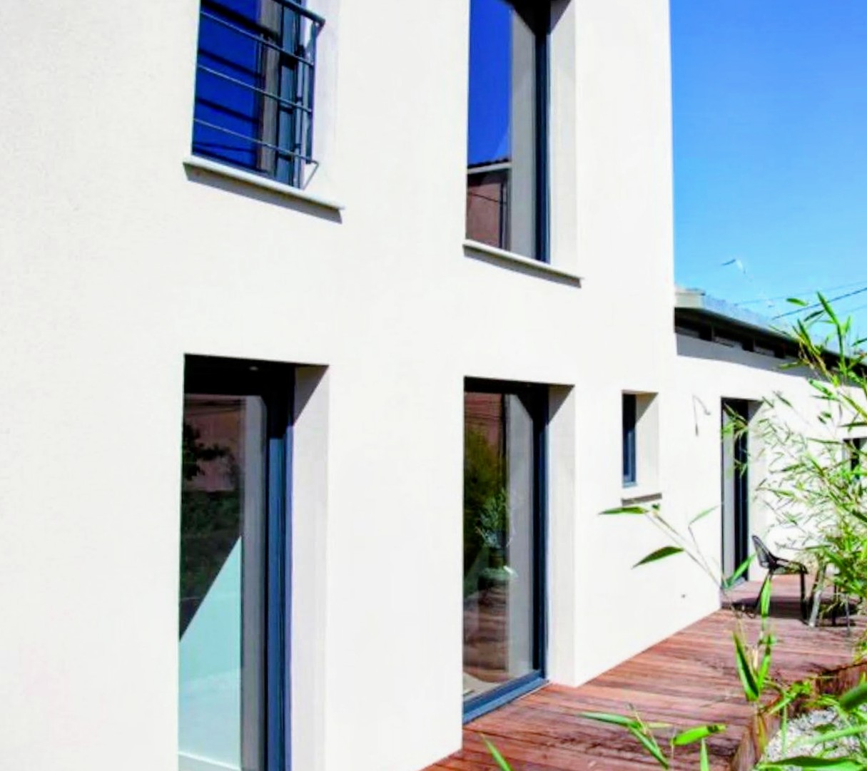 Maison contemporaine à enduit blanc avec baies vitrées toute hauteur en aluminium gris anthracite, terrasse en bois