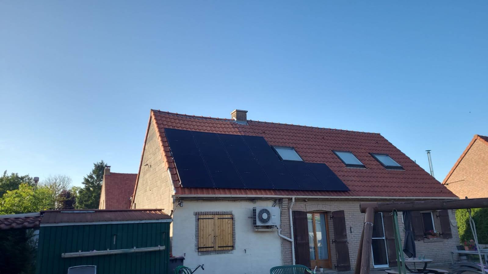Toiture en tuiles rouges équipée de panneaux photovoltaïques noirs et de fenêtres de toit, unité extérieure de climatisation en façade