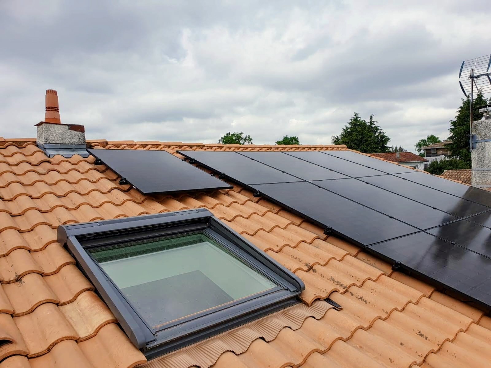Panneaux photovoltaïques posés autour d'une fenêtre de toit sur une couverture en tuiles