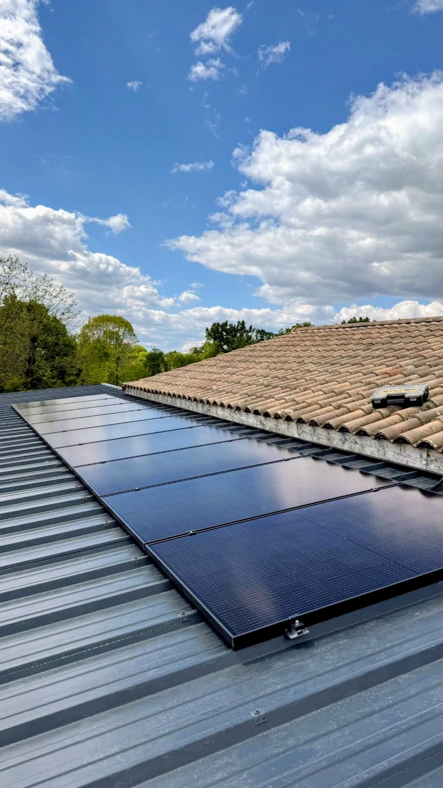 Panneaux photovoltaïques noirs posés sur une couverture en bac acier, accolée à une toiture en tuiles canal anciennes
