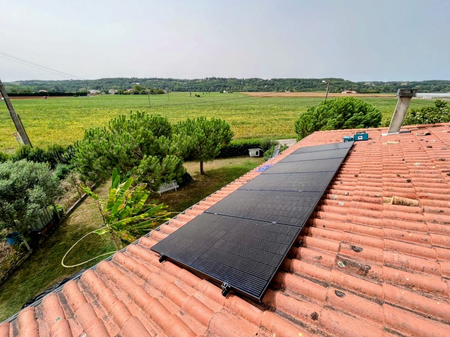 Rangée de panneaux photovoltaïques noirs sur une longue toiture en tuiles face à des champs