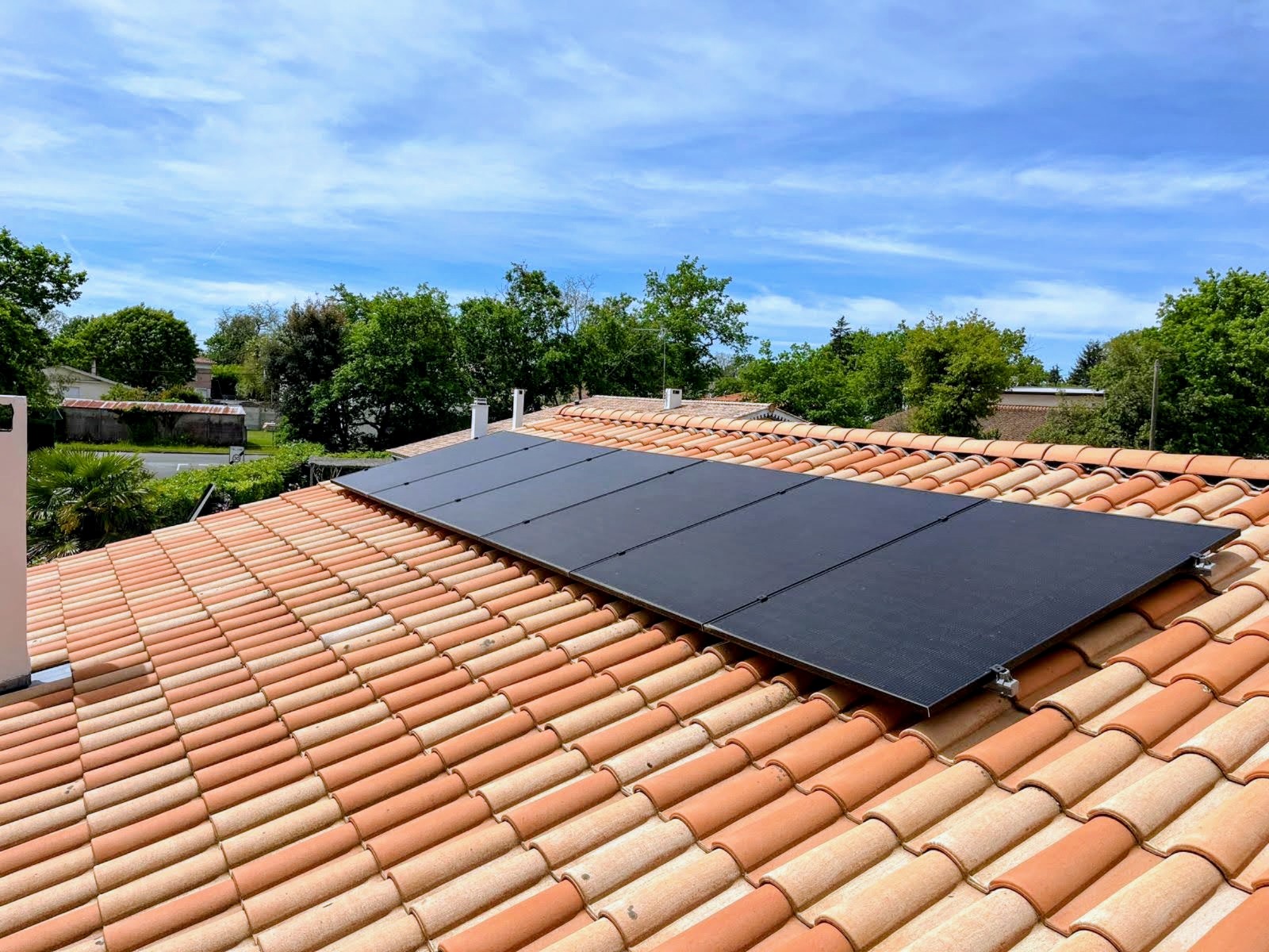 Champ de panneaux photovoltaïques full black posés en surimposition sur une toiture en tuiles canal, ciel bleu et jardin arboré