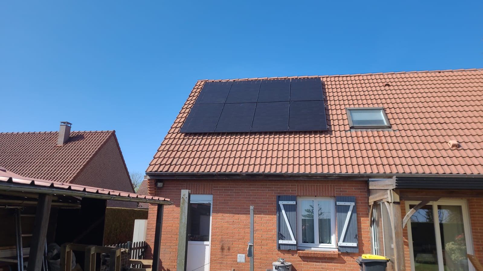 Installation photovoltaïque terminée, huit panneaux noirs alignés sur une toiture en tuiles pannes d'une maison de brique