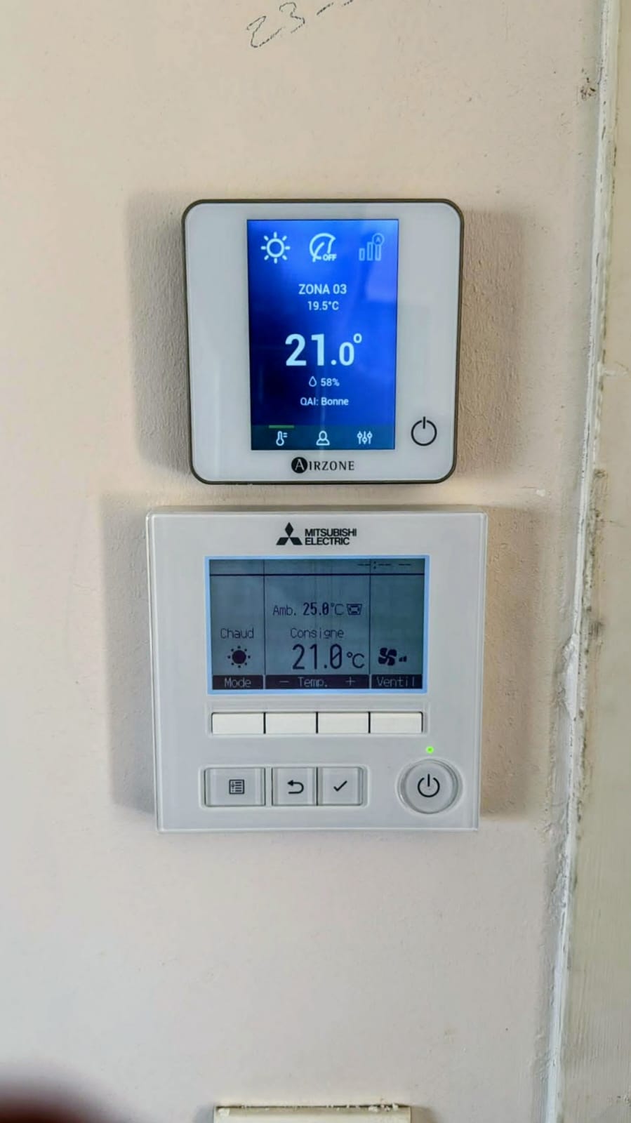 Thermostat Airzone affichant 21 °C et 58 % d'humidité au-dessus d'une télécommande murale Mitsubishi Electric
