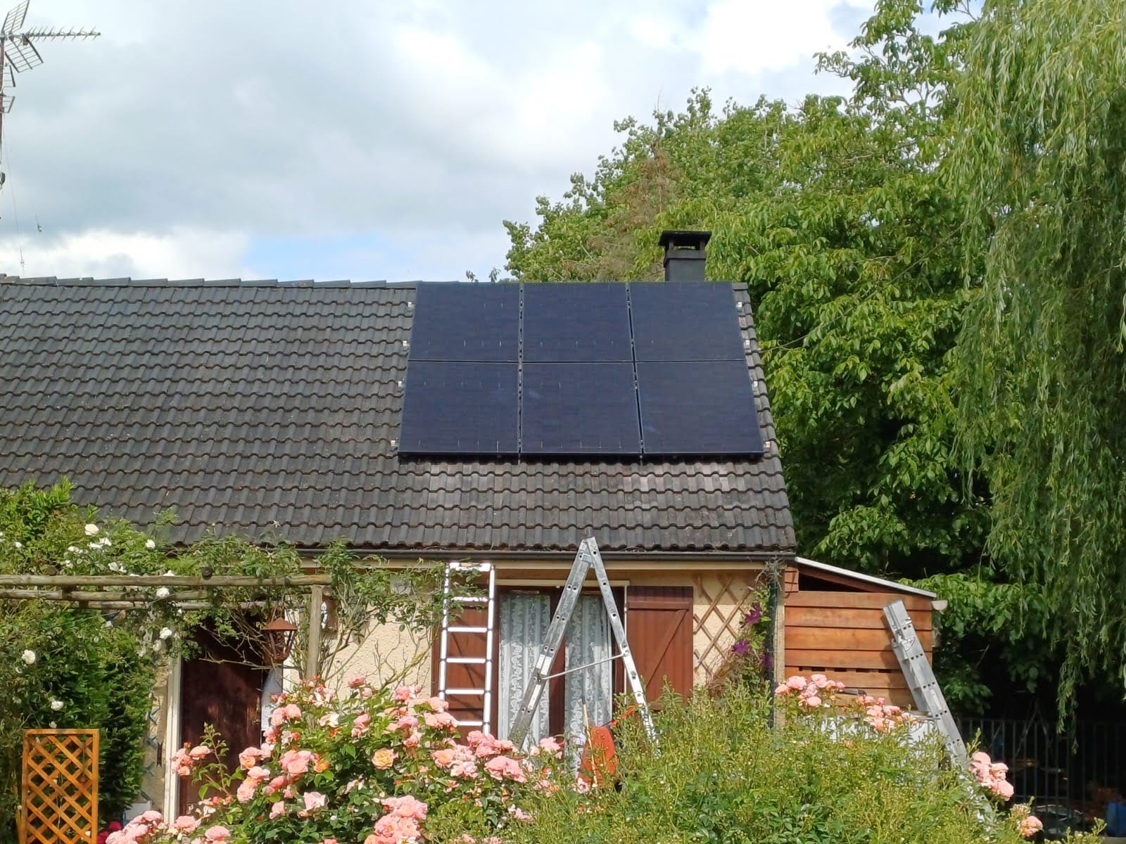 Six panneaux photovoltaïques noirs posés en surimposition sur la toiture en tuiles sombres d'une petite maison