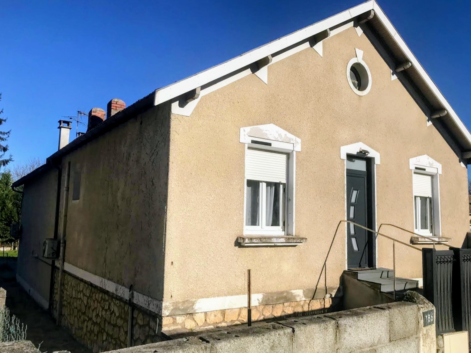 Façade enduite claire avec volets roulants blancs et porte d'entrée anthracite