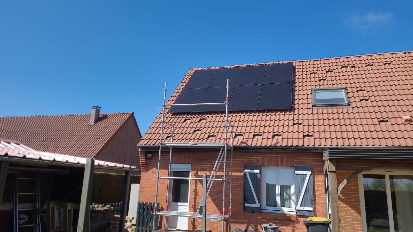Panneaux photovoltaïques noirs en cours de pose sur une toiture en tuiles pannes, échafaudage en place, maison de brique