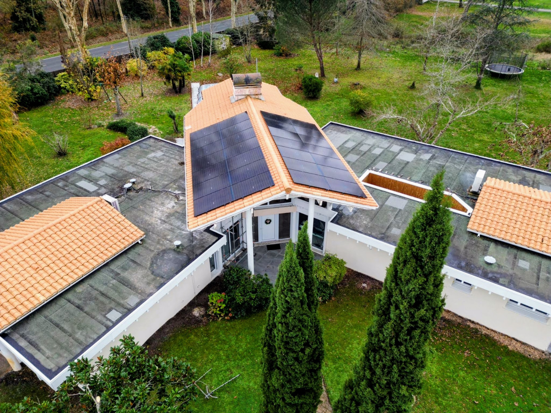 Vue aérienne d'une maison de plain-pied avec deux pans de panneaux photovoltaïques noirs sur toiture tuiles