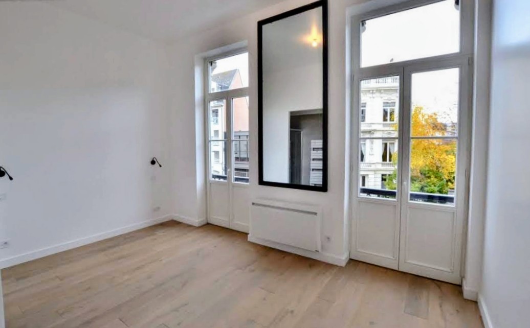 Pièce lumineuse à parquet clair avec grand miroir noir, portes-fenêtres et murs blancs