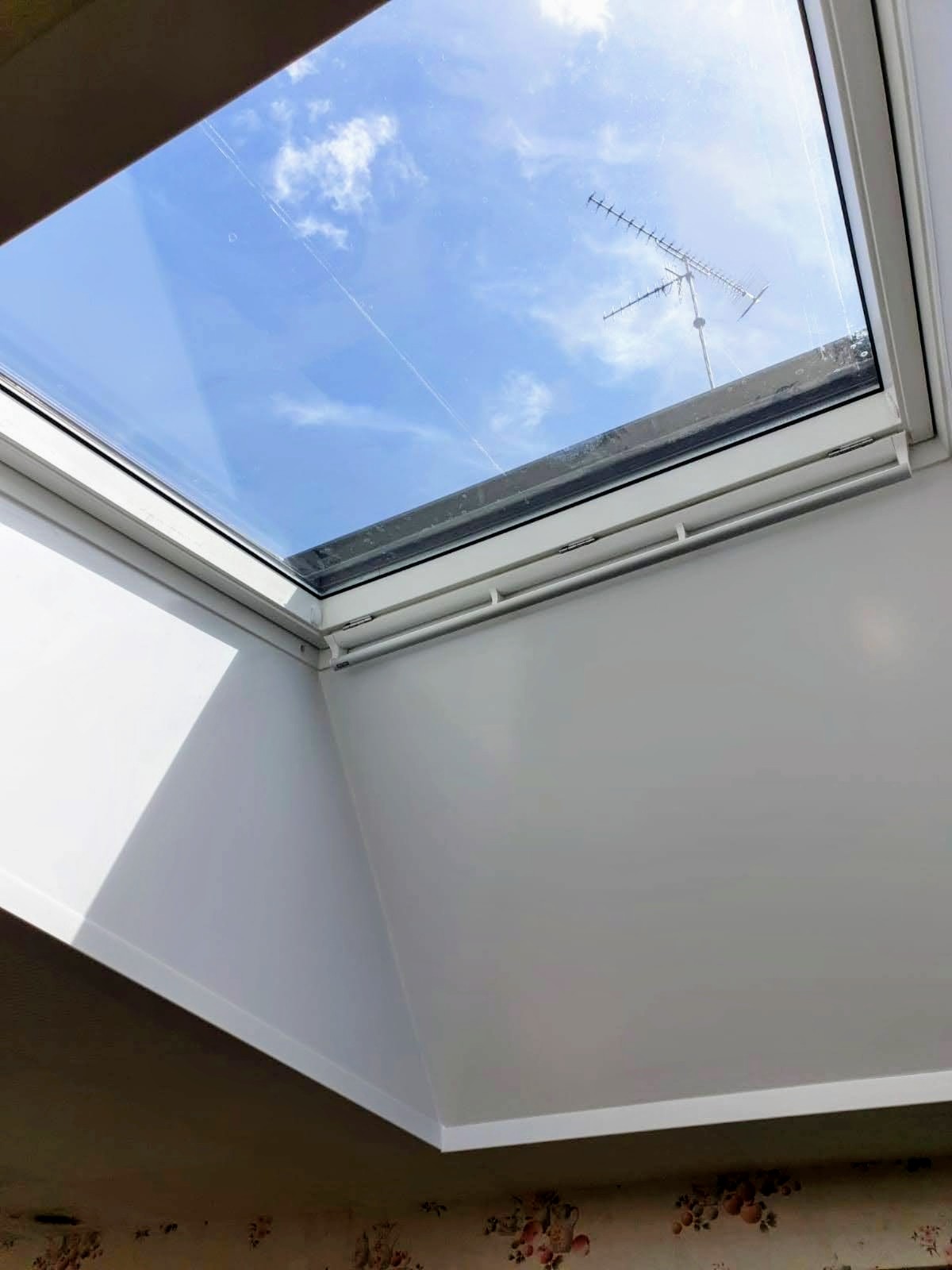 Fenêtre de toit vue de l'intérieur avec store intérieur relevé et rails latéraux, ébrasement blanc